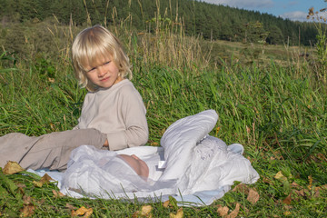 A blond boy with younger newborn brother siiting on a grass during outing