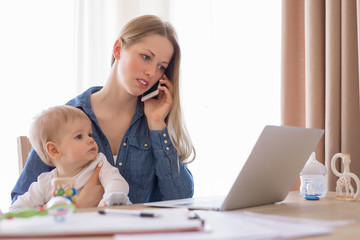 Working mother with baby in her lap working from home © Kaspars Grinvalds