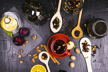 Teas in cans and wooden spoons surrounded by fruit and nut