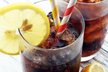 Softdrink with ice cubes, lemon and straw in glass