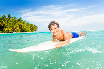 Happy little boy swim on surfing board in the sea