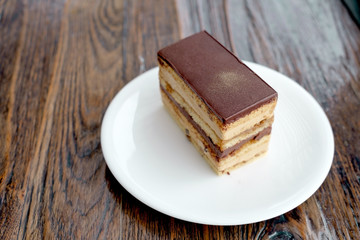 Sweet coffe cake with chocolate layer topping with gold color icing powder in white ceramic plate on the wood floor.