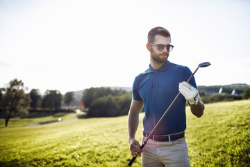 Full length view of man in cap holding golf club and hitting ball on green lawn