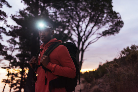 Focused Young African Man Wearing A Headlamp Hiking At Dusk