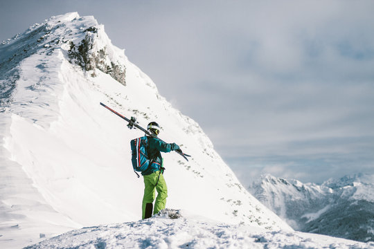 male skier standing alone on top of a snowcovered summit looking to the surrounding peaks