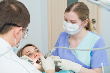 Young woman getting dental treatment , hands of dentist and assistant makes treatment procedures to female patient.