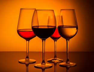 Set of four wine glasses with red, white and rose wine on orange background