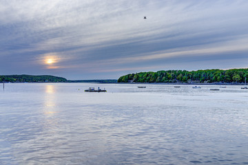 Sunset sun path in Bar Harbor, Maine village with empty boats in water