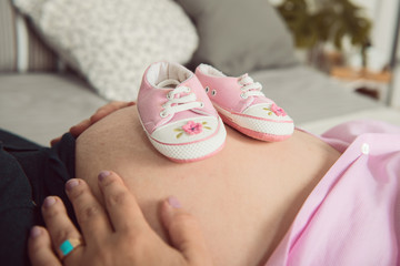 Pregnant girl hugging her belly and holding in her hands boots