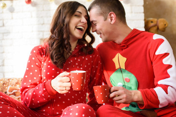 Beautiful kissing pregnant couple in love drinking tea on the background of a Christmas tree, having a rest on Christmas holidays before the new year