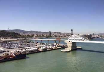 Aerial view of Barcelona port. Big cruise ship is waiting to depart. Many cars and containers to be shipped. Modern bridge and the city are in the view.