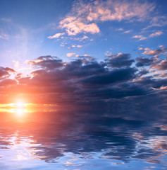 Fototapeta na wymiar The blue sky above the storm clouds at sunset over calm water.