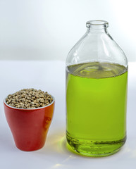 Hemp seeds in a cup and hempseed oil in a glass jar on a white background.