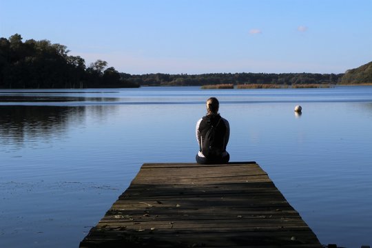 lonely woman sitting on a jetty by the lake, loneliness