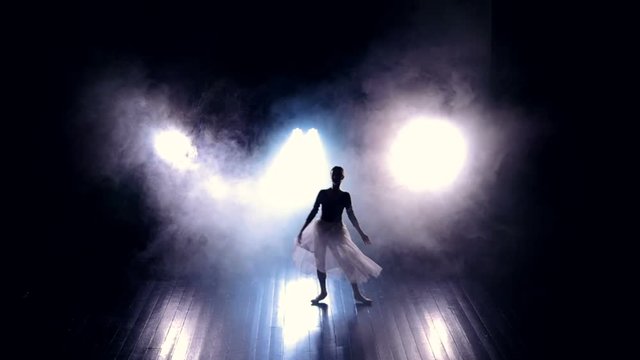 A ballet dancer makes high jumps through a dark stage. 