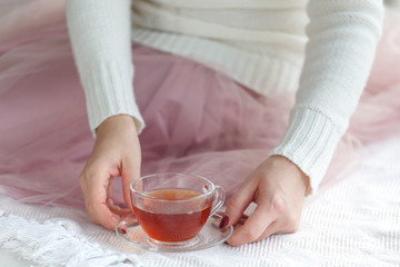 Close up of woman's hands holding a cup of tea, wearing a white sweater and enjoying the leisure time