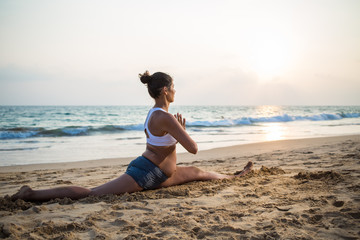 Fototapeta na wymiar Natural looking pregnant woman practicing yoga at the seashore at sunset