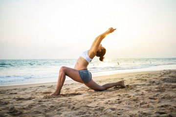 Fototapeta na wymiar Natural looking pregnant woman practicing yoga at the seashore at sunset