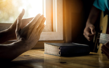 Two man is playing guitar and sing a song from Christian hymn book with bible on wooden table