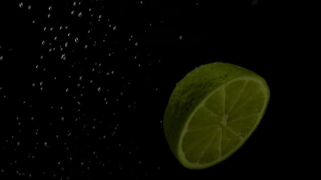 Slo-motion whole lemon and lime falling on water