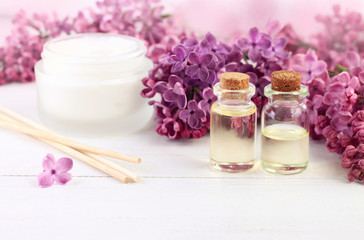 Obraz na płótnie Canvas Aromatic botanical spa treatment. Bottles of essential oil, fresh lilac blossom, skincare cream, soft pink light background. 