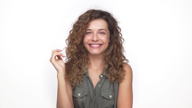 young pretty lady with long curly hair smiling being shy on camera over white background. Concept of emotions