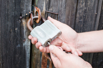 Dirty hand of man with key unlocking the padlock on the wood door of the hangar
