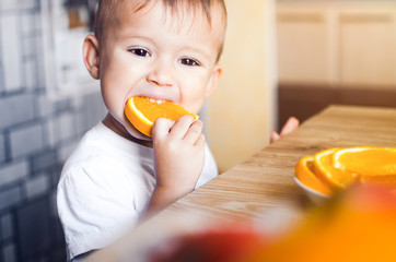 The child in the kitchen eating an orange