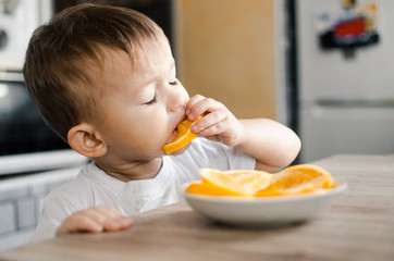 The child in the kitchen eating an orange