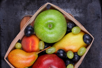 Red apple, dark blue grapes, green apple, yellow pear, green grapes, orange peach in a wooden box on a metallic background in retro style