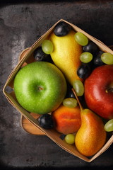 Red apple, dark blue grapes, green apple, yellow pear, green grapes, orange peach in a wooden box on a metallic background in retro style