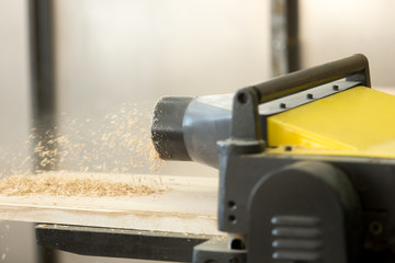 Close up photo of stationary powerful woodworking machine tool throwing out sawdust while reducing thickness of hardwood board. Producing lumber and billets for wooden furniture manufacturing, joinery