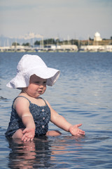 Cute Baby Girl with White Bonnet Playing in Lake