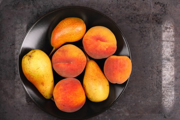 Pears and peaches on a black plate in retro style for a designer on a metal old background