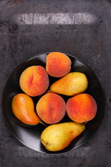 Pears and peaches on a black plate in retro style for a designer on a metal old background