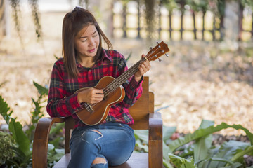 Fototapeta na wymiar Young hipster woman sitting playing ukulele guitar at home in garden.