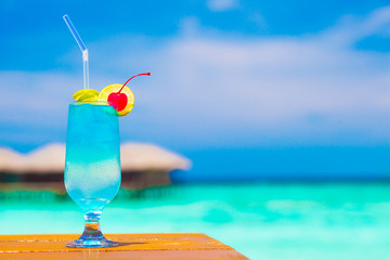 glass of blue curacao cocktail with cherry by the beach