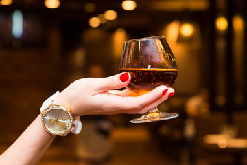 The girl's hand holds a glass of cognac