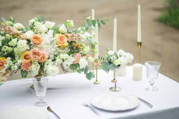 decorated wedding table for two with beautiful flower composition, glasses for wine, candles and plates, outdoor, fine art.