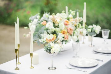 decorated wedding table for two with beautiful flower composition, glasses for wine, candles and plates, outdoor, fine art.