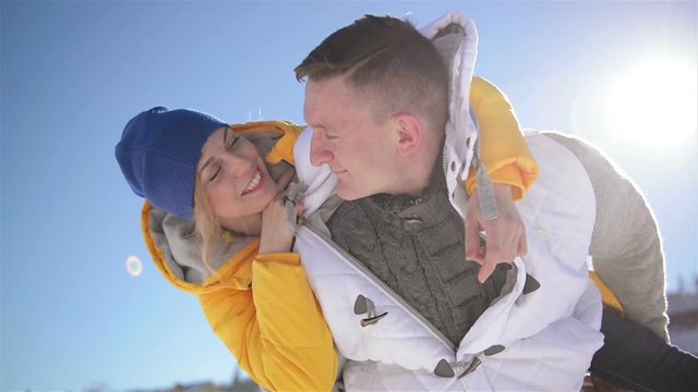 Pretty Blonde Woman is Hugging Handsome Man Sitting on His Shoulders During Winter Vacation in the Mountains. Closeup Portrait of Man and Woman in Love.