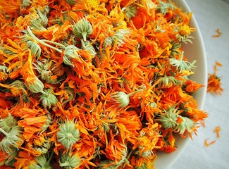 Dry calendula marigold flowers in a bowl on white linen napkin.