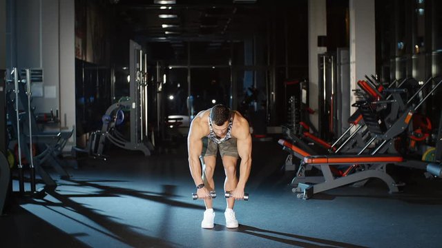 Beautiful muscular man workout and lifts hands with dumbbells in gym