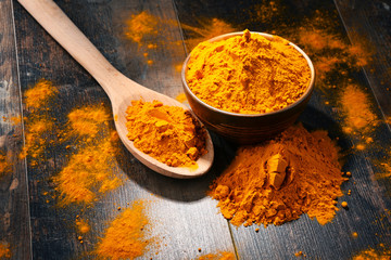 Composition with bowl of turmeric powder on wooden table