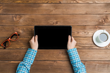 Top view of woman sitting at wooden table and working with tablet