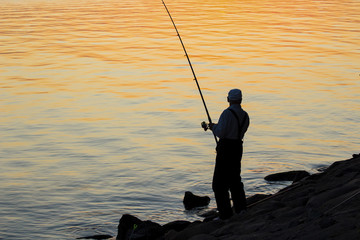 man is fishing on the beach at sunset