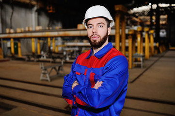 Cute young worker in a white construction helmet against a background of a factory or production