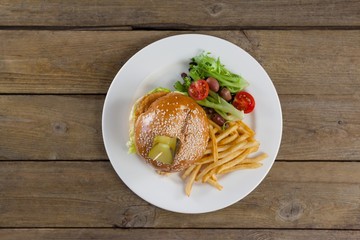 Hamburger, french fries and salad in plate on wooden table