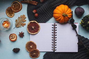 Cozy autumn background, notebook, decorative pumpkins, dried oranges, candle, nuts, cinnamon and autumn leaves