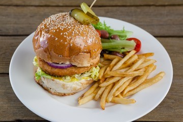 Hamburger, french fries and salad in plate on wooden table